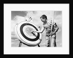 1960s boy jeans striped t-shirt holding bow & pulling arrow out of target bull's-eye by Anonymous