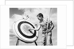 1960s boy jeans striped t-shirt holding bow & pulling arrow out of target bull's-eye by Anonymous