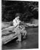 1920s 1930s woman sitting on rock by side of stream wearing waders putting fly on tippet by Anonymous