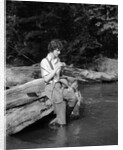 1920s 1930s woman sitting on rock by side of stream wearing waders putting fly on tippet by Anonymous