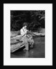 1920s 1930s woman sitting on rock by side of stream wearing waders putting fly on tippet by Anonymous