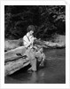 1920s 1930s woman sitting on rock by side of stream wearing waders putting fly on tippet by Anonymous