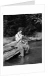 1920s 1930s woman sitting on rock by side of stream wearing waders putting fly on tippet by Anonymous