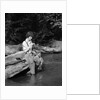 1920s 1930s woman sitting on rock by side of stream wearing waders putting fly on tippet by Anonymous