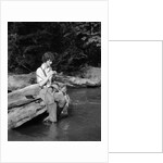 1920s 1930s woman sitting on rock by side of stream wearing waders putting fly on tippet by Anonymous