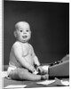 1950s 1960s baby in diaper sticking out tongue holding glasses sitting before adding machine looking at camera by Anonymous