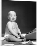 1950s 1960s baby in diaper sticking out tongue holding glasses sitting before adding machine looking at camera by Anonymous