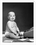1950s 1960s baby in diaper sticking out tongue holding glasses sitting before adding machine looking at camera by Anonymous