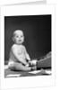 1950s 1960s baby in diaper sticking out tongue holding glasses sitting before adding machine looking at camera by Anonymous