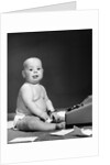1950s 1960s baby in diaper sticking out tongue holding glasses sitting before adding machine looking at camera by Anonymous