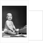 1950s 1960s baby in diaper sticking out tongue holding glasses sitting before adding machine looking at camera by Anonymous