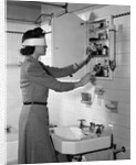 1940s woman wearing blindfold reaching into bathroom medicine cabinet by Anonymous