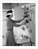 1940s woman wearing blindfold reaching into bathroom medicine cabinet by Anonymous