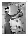 1940s woman wearing blindfold reaching into bathroom medicine cabinet by Anonymous
