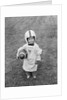 1950s boy standing in grass wearing oversized shirt & helmet holding football by Anonymous