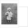 1950s boy standing in grass wearing oversized shirt & helmet holding football by Anonymous