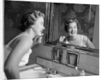 1950s smiling woman looking into bathroom mirror brushing teeth by Anonymous
