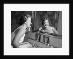 1950s smiling woman looking into bathroom mirror brushing teeth by Anonymous