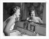 1950s smiling woman looking into bathroom mirror brushing teeth by Anonymous
