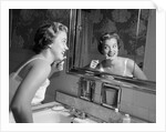 1950s smiling woman looking into bathroom mirror brushing teeth by Anonymous
