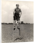 1930s 1940s smiling happy boy wearing striped shirt & short pants walking on pair of stilts looking at camera by Anonymous