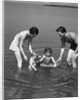 1930s family father mother daughter son with rubber inner tube wading in seashore water by Anonymous