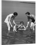 1930s family father mother daughter son with rubber inner tube wading in seashore water by Anonymous