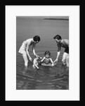 1930s family father mother daughter son with rubber inner tube wading in seashore water by Anonymous