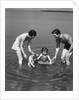 1930s family father mother daughter son with rubber inner tube wading in seashore water by Anonymous