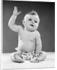 1950s portrait of baby sitting one arm raised waving by Anonymous
