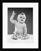 1950s portrait of baby sitting one arm raised waving by Anonymous