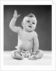 1950s portrait of baby sitting one arm raised waving by Anonymous