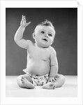 1950s portrait of baby sitting one arm raised waving by Anonymous