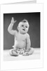 1950s portrait of baby sitting one arm raised waving by Anonymous