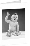 1950s portrait of baby sitting one arm raised waving by Anonymous