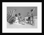 1960s at the beach two boys with baseball bat trying to pull up father seated next to mother so he will play with them by Anonymous