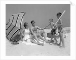1960s at the beach two boys with baseball bat trying to pull up father seated next to mother so he will play with them by Anonymous