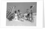 1960s at the beach two boys with baseball bat trying to pull up father seated next to mother so he will play with them by Anonymous