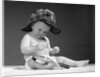 1960s baby in diaper wearing sherlock holmes deerstalker style double-billed cap with magnifying glass resting on leg inspecting a clue by Anonymous