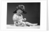 1960s baby in diaper wearing sherlock holmes deerstalker style double-billed cap with magnifying glass resting on leg inspecting a clue by Anonymous