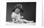 1960s baby in diaper wearing sherlock holmes deerstalker style double-billed cap with magnifying glass resting on leg inspecting a clue by Anonymous