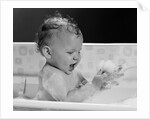 1960s baby in bathtub playing with suds indoor by Anonymous