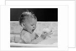 1960s baby in bathtub playing with suds indoor by Anonymous