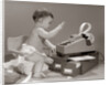 1960s baby seated in small chair hitting keys on office adding machine on top of small file drawers by Anonymous
