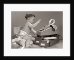 1960s baby seated in small chair hitting keys on office adding machine on top of small file drawers by Anonymous