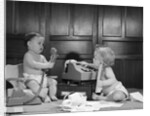 1960s 2 babies in diapers one on chair with telephone other on floor with adding machine pencil behind ear by Anonymous