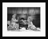 1960s 2 babies in diapers one on chair with telephone other on floor with adding machine pencil behind ear by Anonymous