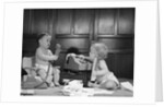 1960s 2 babies in diapers one on chair with telephone other on floor with adding machine pencil behind ear by Anonymous