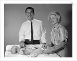 1960s smiling mother and father with twin babies on diaper changing table looking at camera by Anonymous