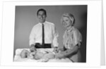 1960s smiling mother and father with twin babies on diaper changing table looking at camera by Anonymous